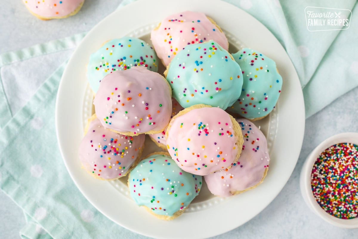 Italian Easter cookies frosted with purple, pink and blue icing and sprinkles stacked together on a plate.