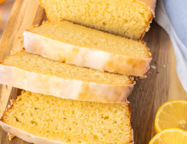 Glazed lemon pound cake sliced on a wooden cutting board.