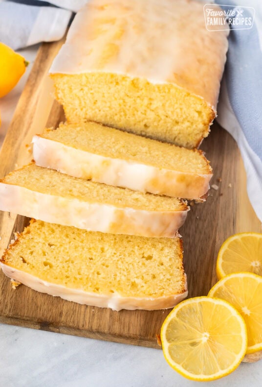 Glazed lemon pound cake sliced on a wooden cutting board.