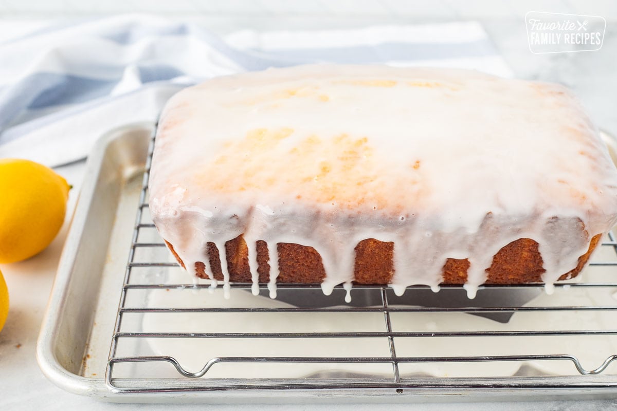 Glaze dripping off the sides of lemon pound cake onto a cookie sheet.