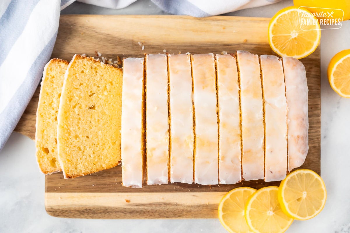 Sliced lemon pound cake on a wooden cutting board surrounded by fresh lemons.