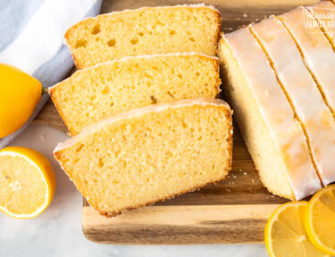 Cutting board with slices of lemon pound cake surrounded by fresh lemons.