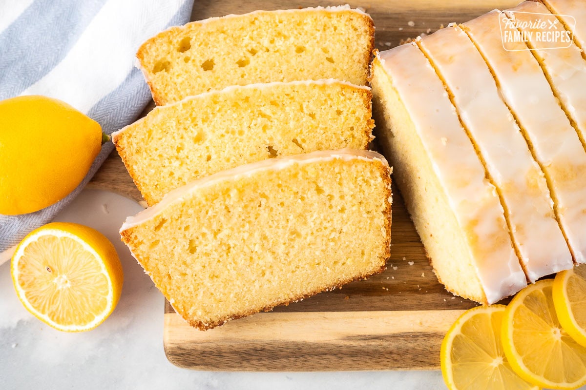 Cutting board with slices of lemon pound cake surrounded by fresh lemons.