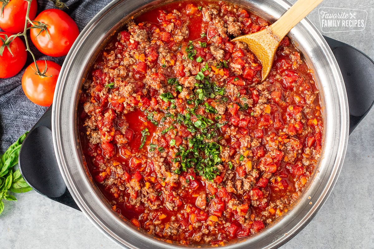 Fresh chopped basil added to a rich spaghetti sauce in a large skillet.