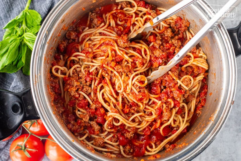 Tossing spaghetti pasta with Italian spaghetti meat sauce with tongs.