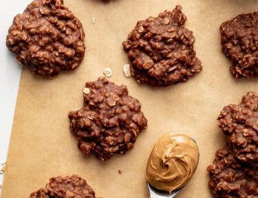 No bake cookies on brown parchment paper with a spoon of peanut butter next to them