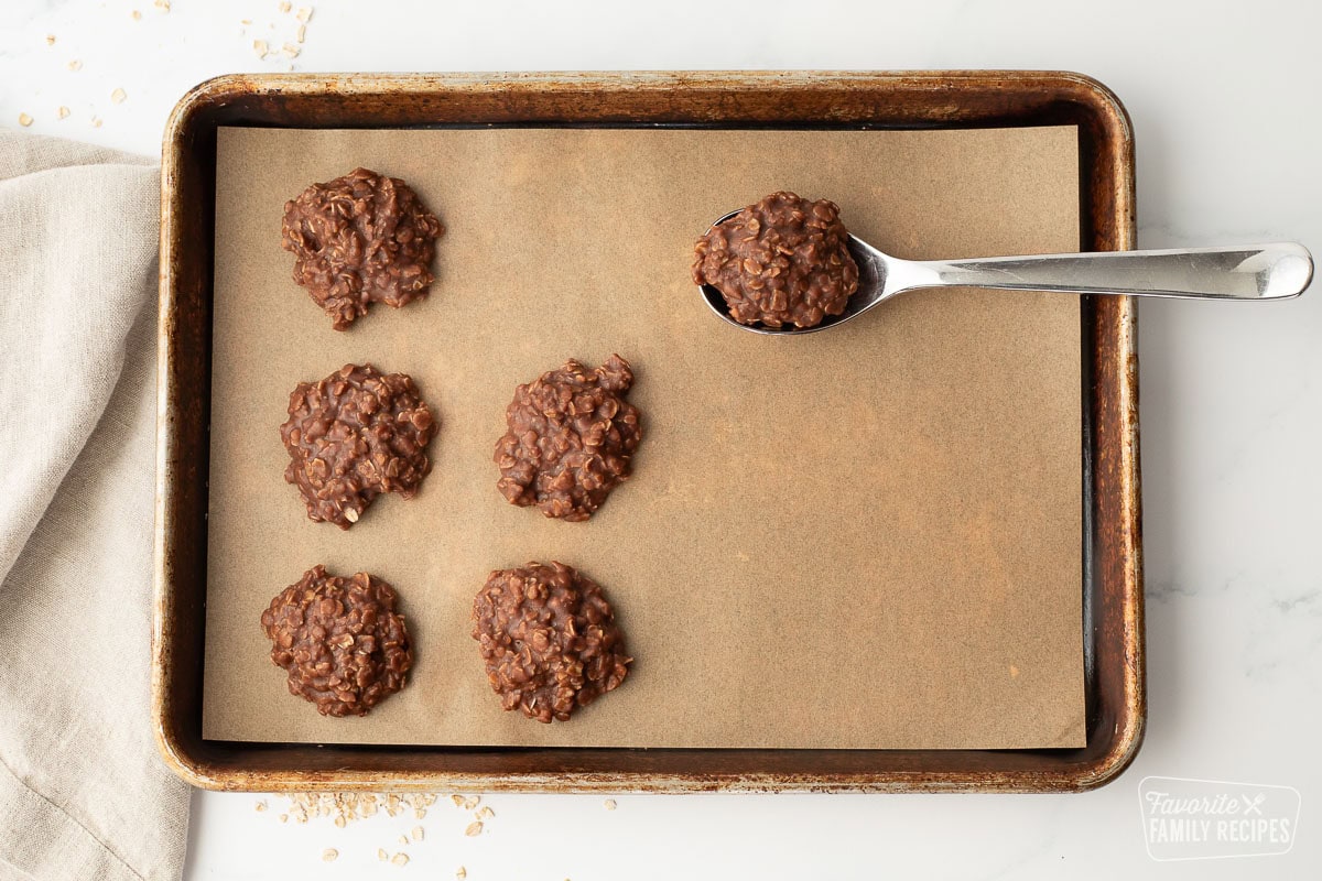 A baking sheet with scoops of chocolate peanut butter no bake cookies with a spoonful being placed on the pan