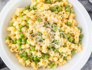 Pasta with peas in a small bowl with fresh grated cheese and pepper.