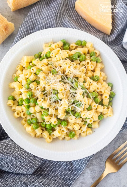 Pasta with peas in a small bowl with fresh grated cheese and pepper.