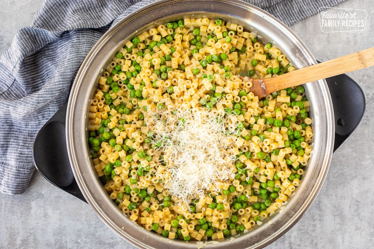 Adding cheese to pasta with peas in a skillet.