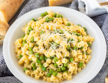 Pasta with peas in a small bowl with fresh grated cheese and pepper.