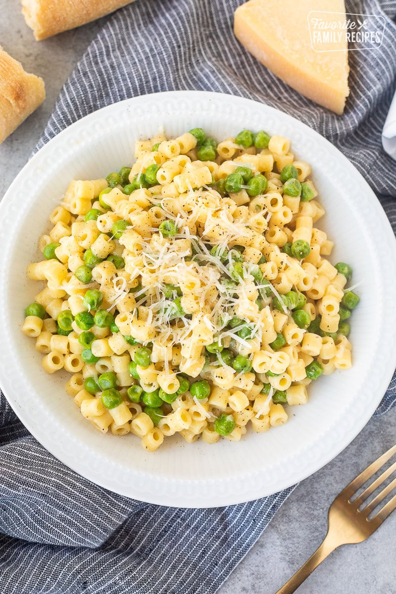 Pasta with peas in a small bowl with fresh grated cheese and pepper.