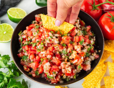 Dipping a chip into a bowl of Pico de Gallo with fresh cut tomatoes, onion, cilantro and jalapeño.