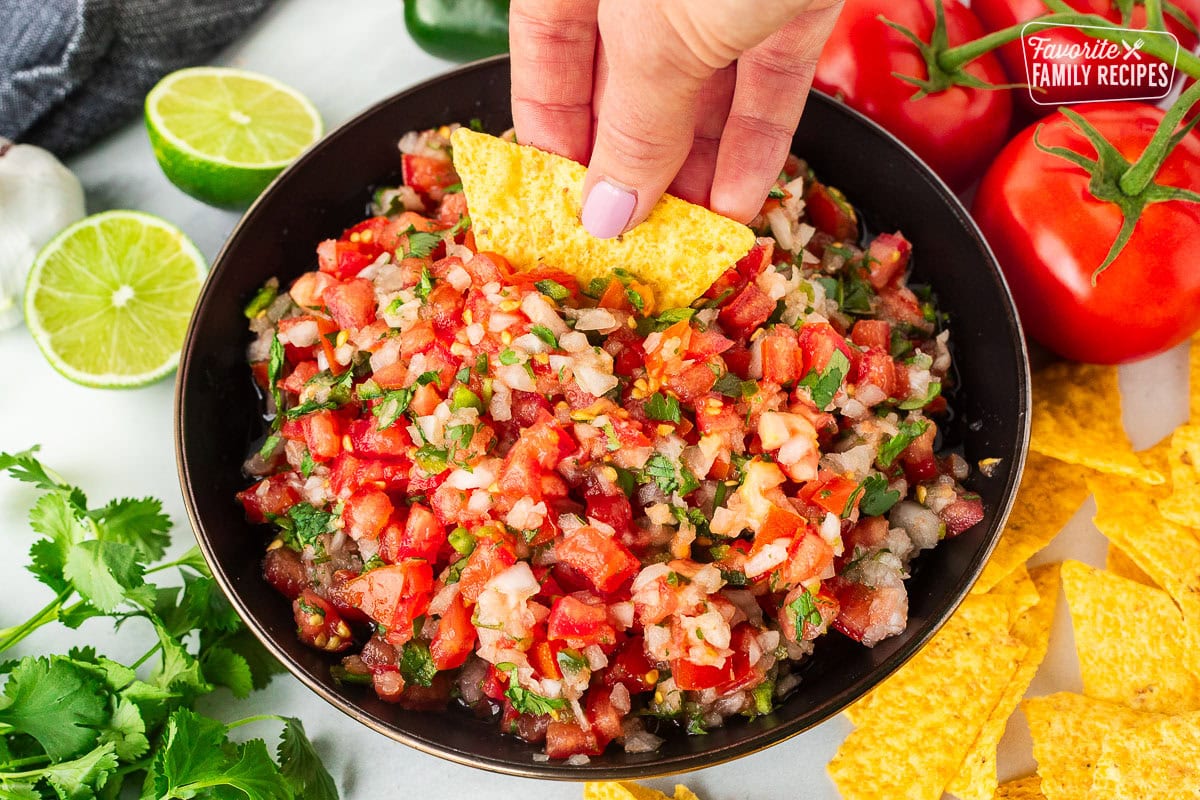 Dipping a chip into a bowl of Pico de Gallo with fresh cut tomatoes, onion, cilantro and jalapeño.