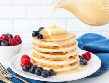 Homemade buttermilk syrup pouring onto a stack of pancakes with fresh blueberries and raspberries.