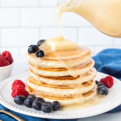 Homemade buttermilk syrup pouring onto a stack of pancakes with fresh blueberries and raspberries.