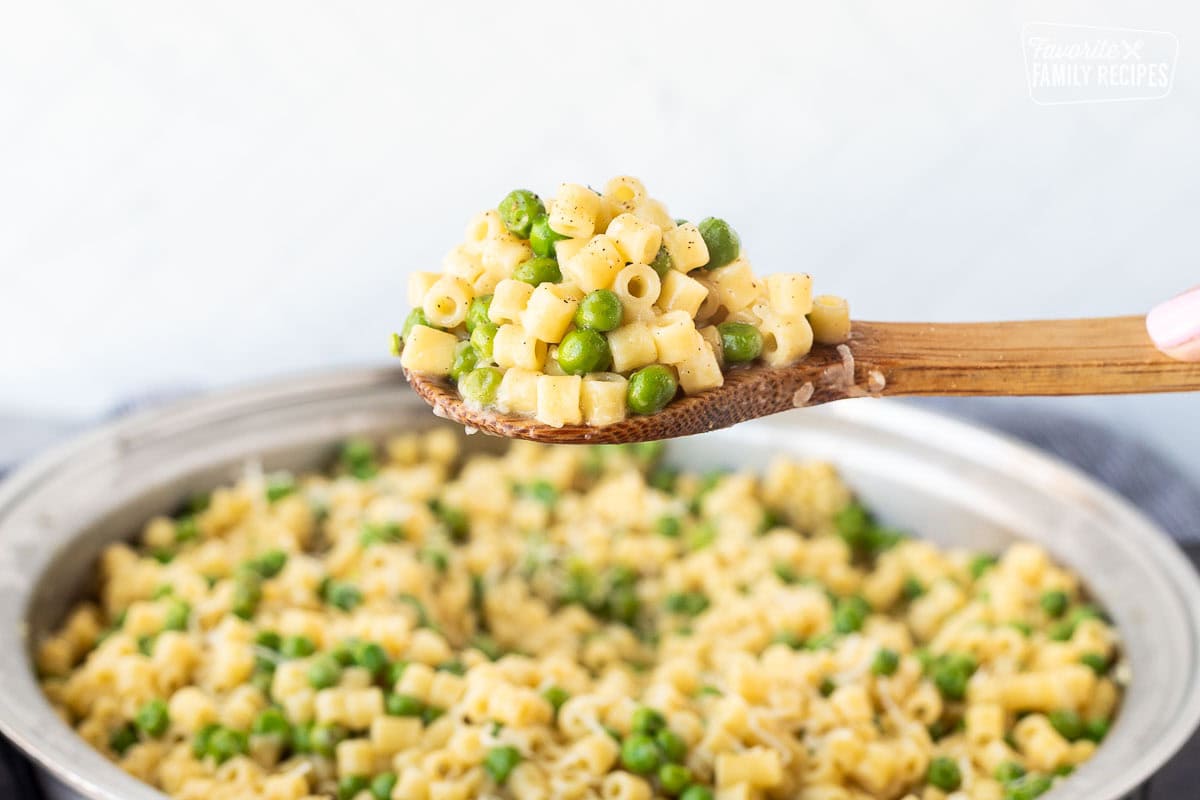 Wooden spoon with a scoop of pasta with peas.