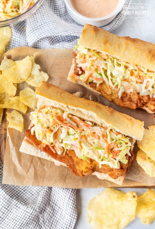 Two Cajun Fried Chicken Po'Boys on a cutting board with chips.