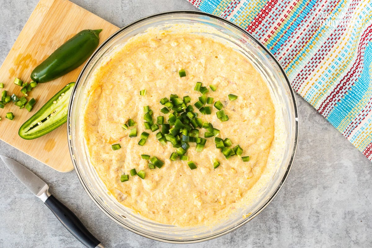 Glass mixing bowl with Mexican cornbread batter and diced jalapeños.