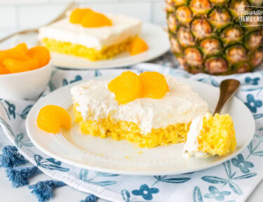 Slice of orange pineapple cake on a plate with a fork and topped with mandarin oranges.