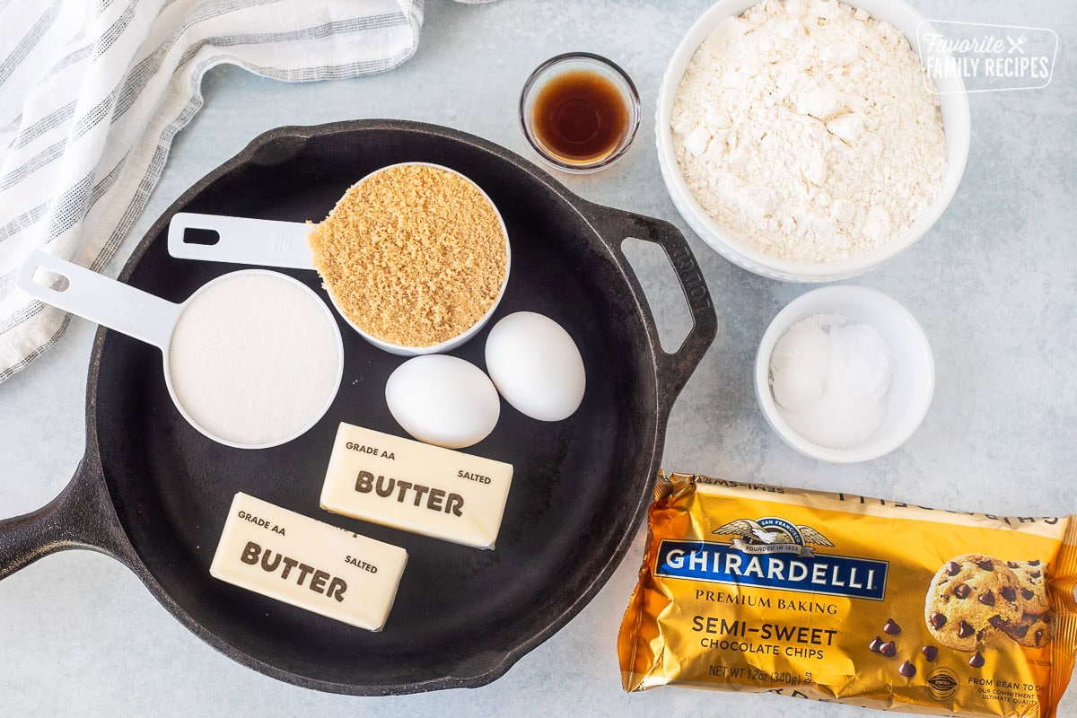 Pizookie ingredients: butter, sugar, eggs, vanilla, flour, baking soda, and chocolate chips, arranged in a cast iron skillet and bowls on a light surface.