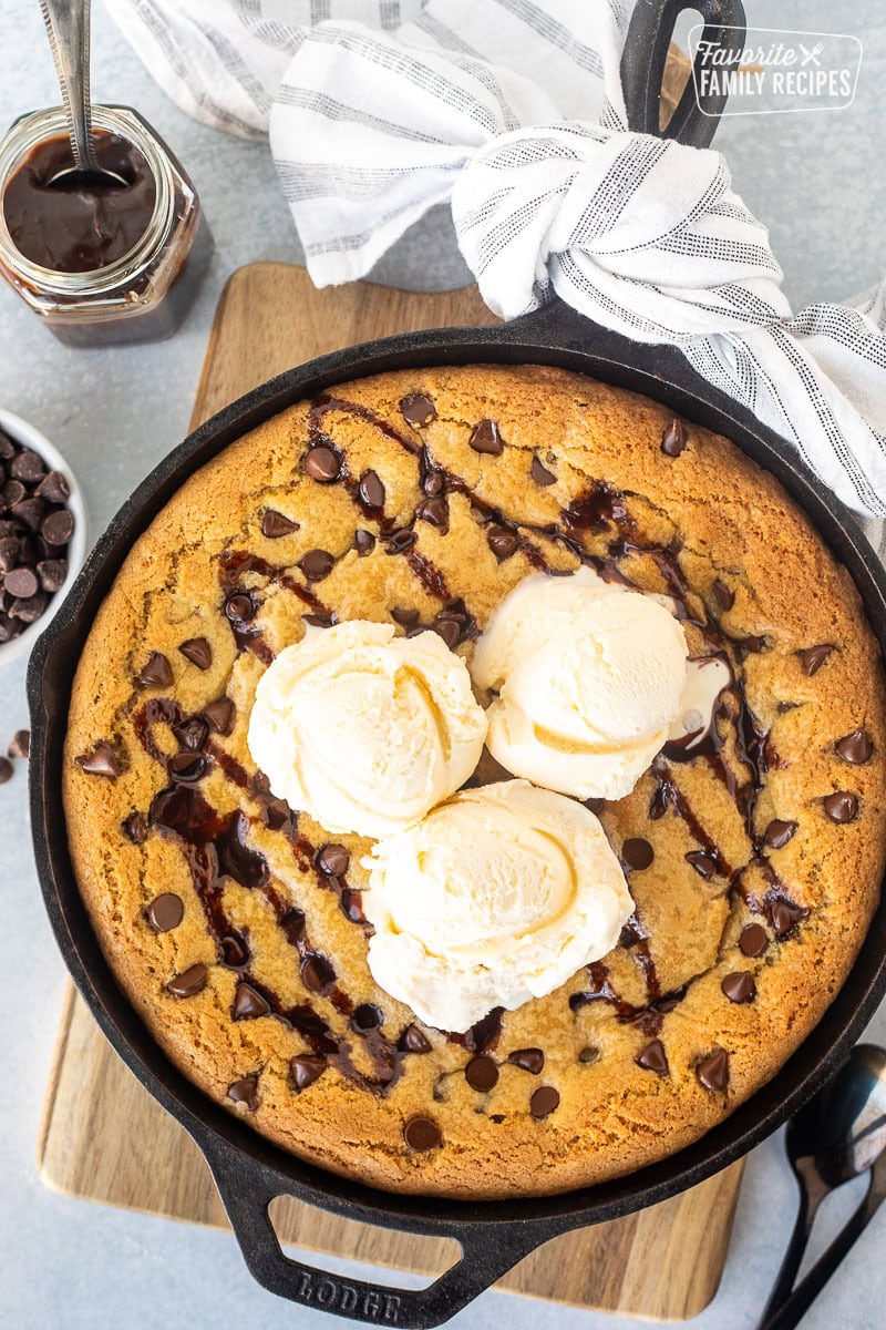 Chocolate chip Pizookie with chocolate sauce in a skillet with three scoops of vanilla ice cream in the center.