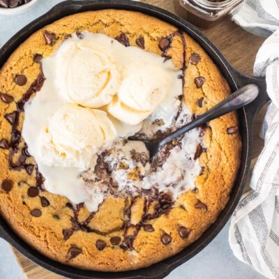 Pizookie with melty ice cream in a skillet with a spoon.