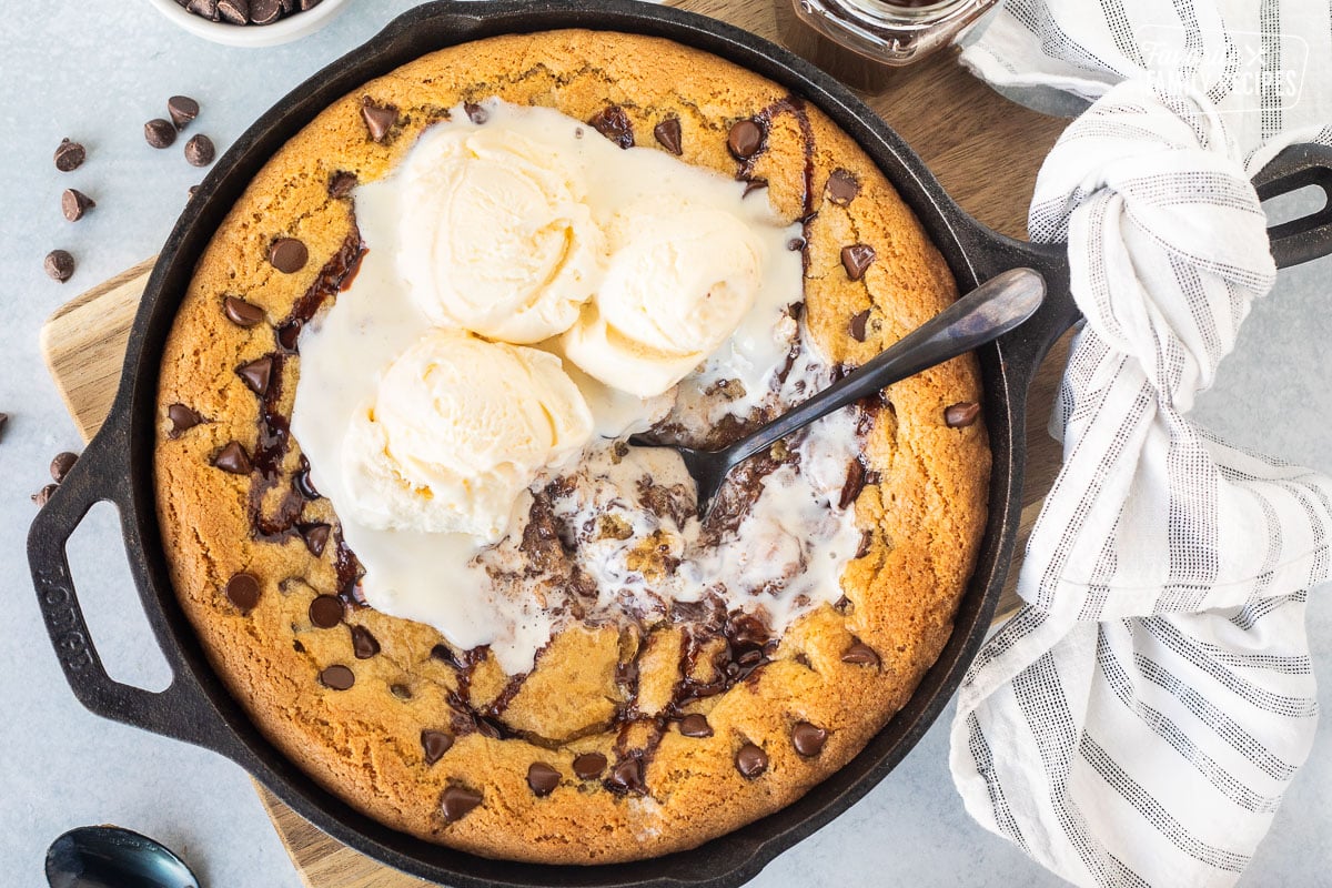 Chocolate chip skillet cookie (Pizookie) with vanilla ice cream melting on top, in a cast iron pan.