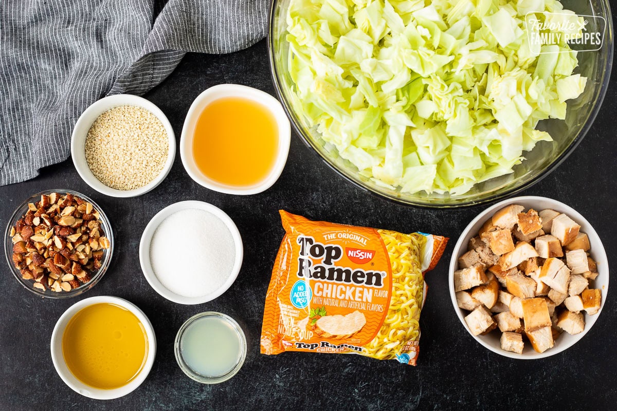 Ingredients to make Ramen Noodle Salad (Pai Mai) including cabbage, Ramen noodles, teriyaki chicken, apple cider vinegar, sesame seeds, roasted almonds, sugar, lemon juice and olive oil.