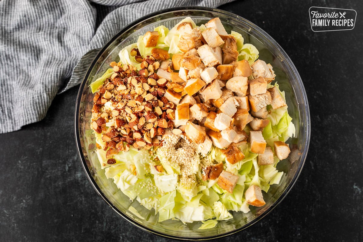 Bowl of cabbage, cut teriyaki chicken, chopped almonds and sesame seeds.