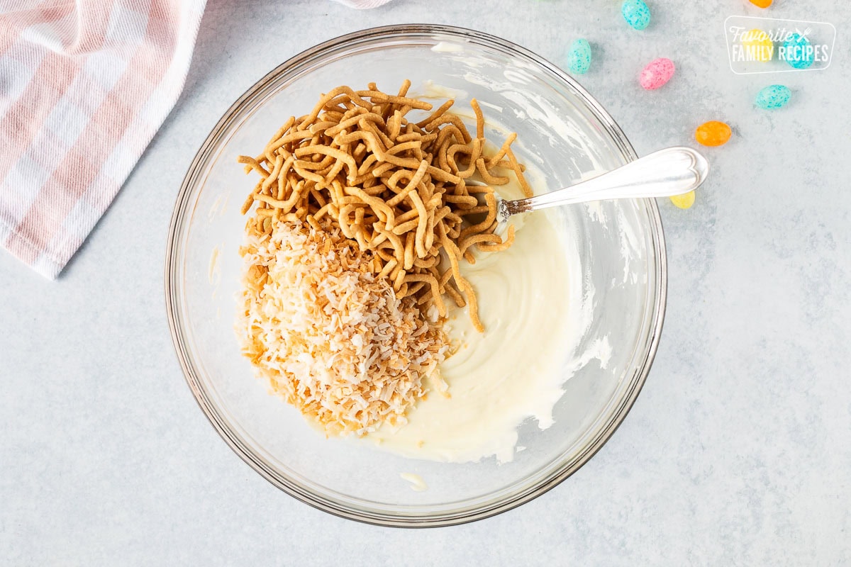 Mixing bowl with melted white chocolate chips, chow mien noodles and toasted coconut.